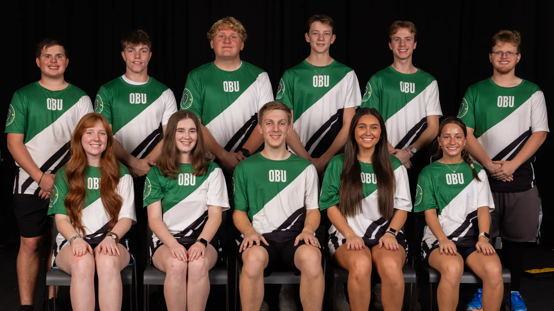 Twelve members of the Tennis Club pose together in two rows, wearing green and white OBU jerseys.