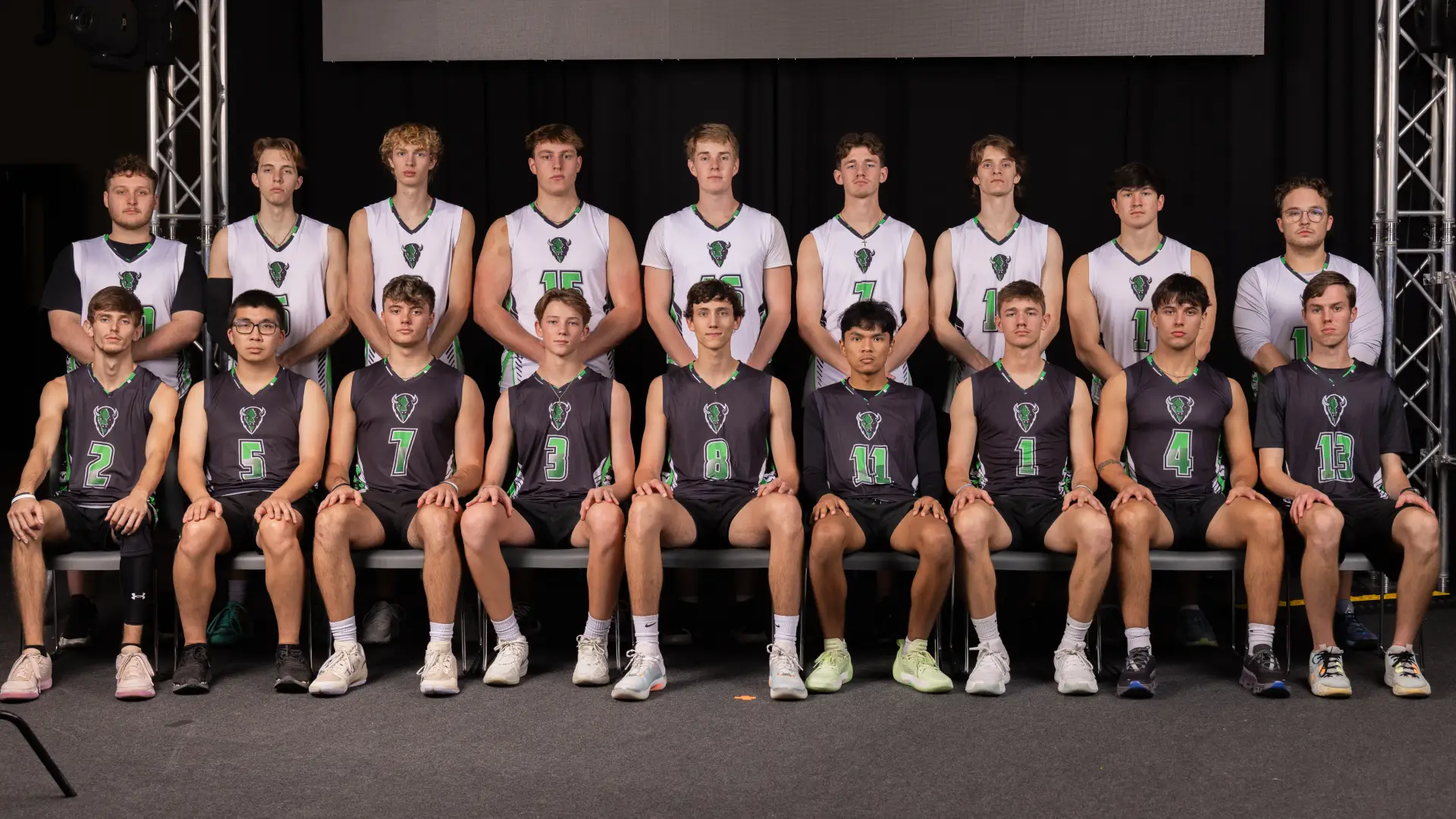 Sixteen members of the Men's Volleyball Club pose together in two rows, wearing white and dark green numbered jerseys with a bison logo.